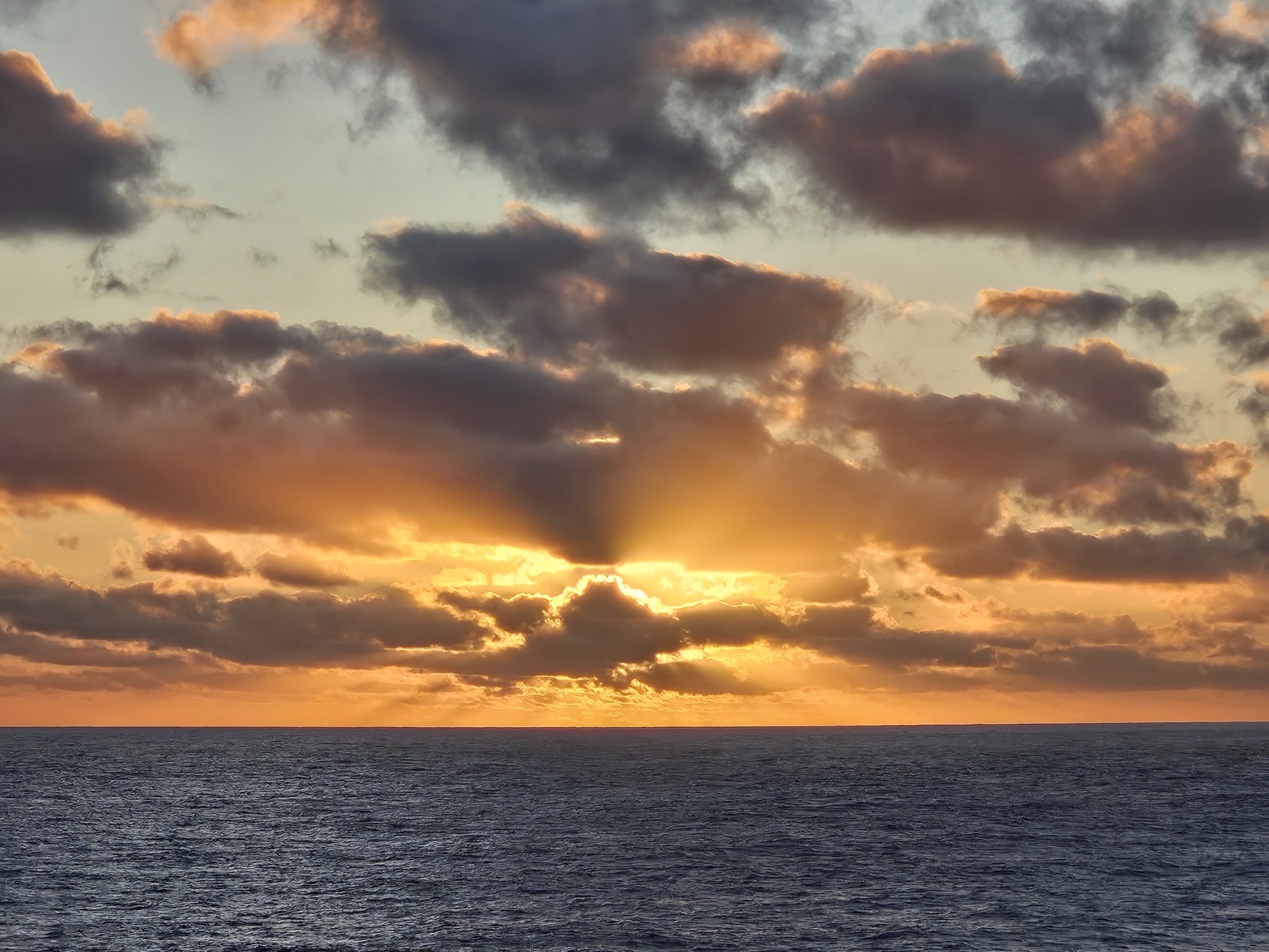 Sunrise breaking through cloud over a calm ocean horizon.